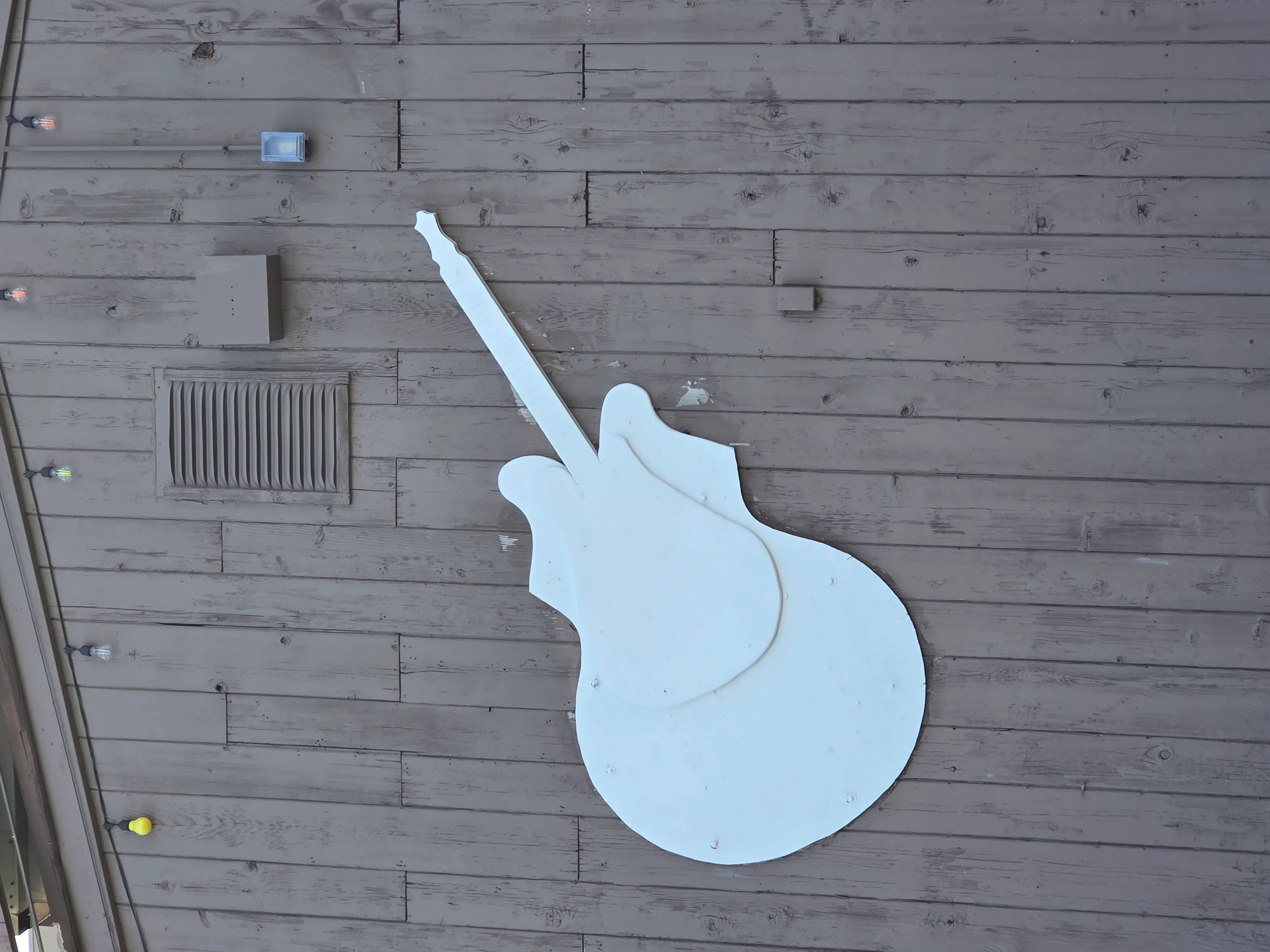 White guitar-shaped sign mounted on gray shiplap wall with vent register