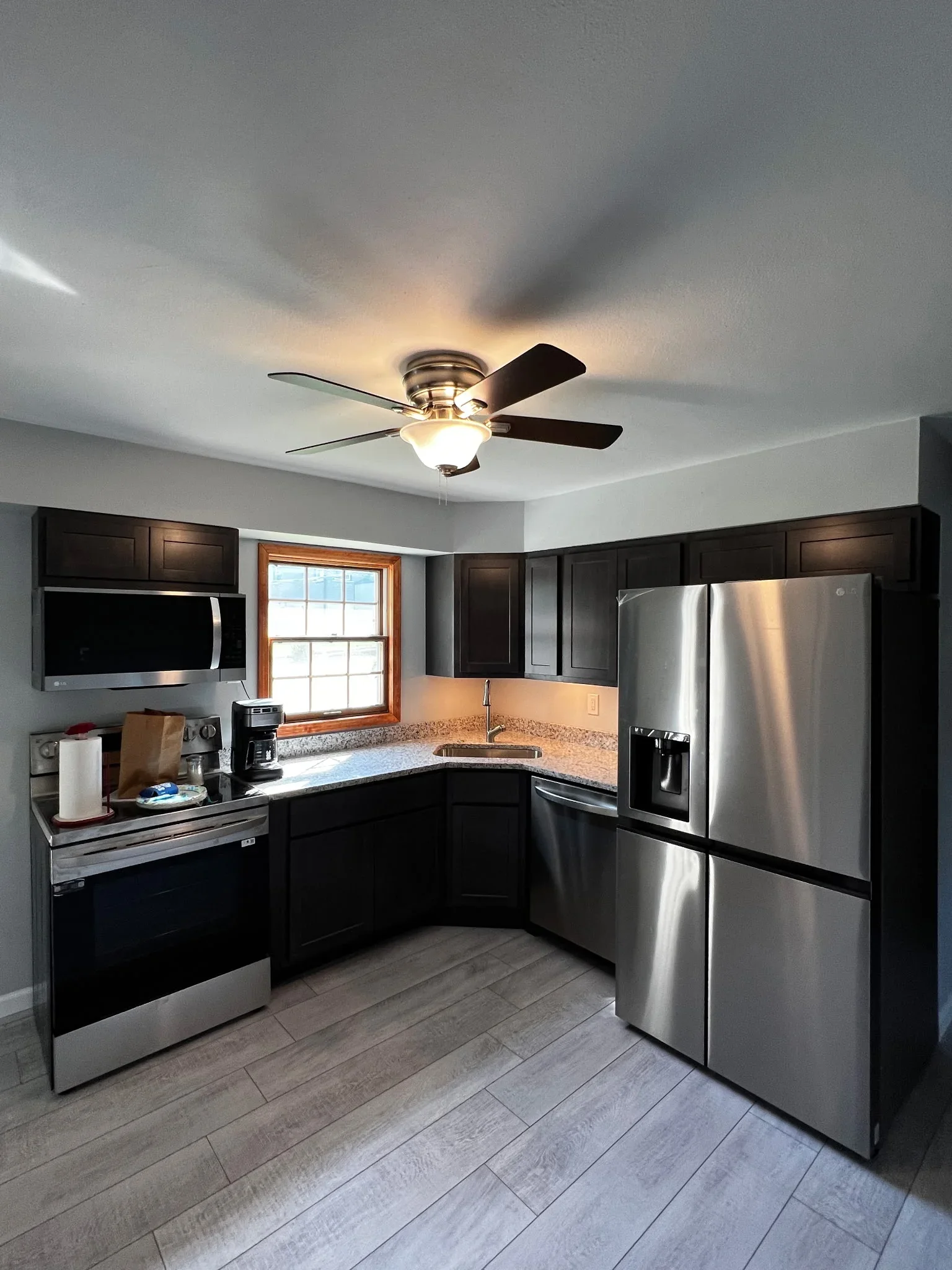 Black cabinetry kitchen with stainless steel appliances, granite counters, and wood-framed window