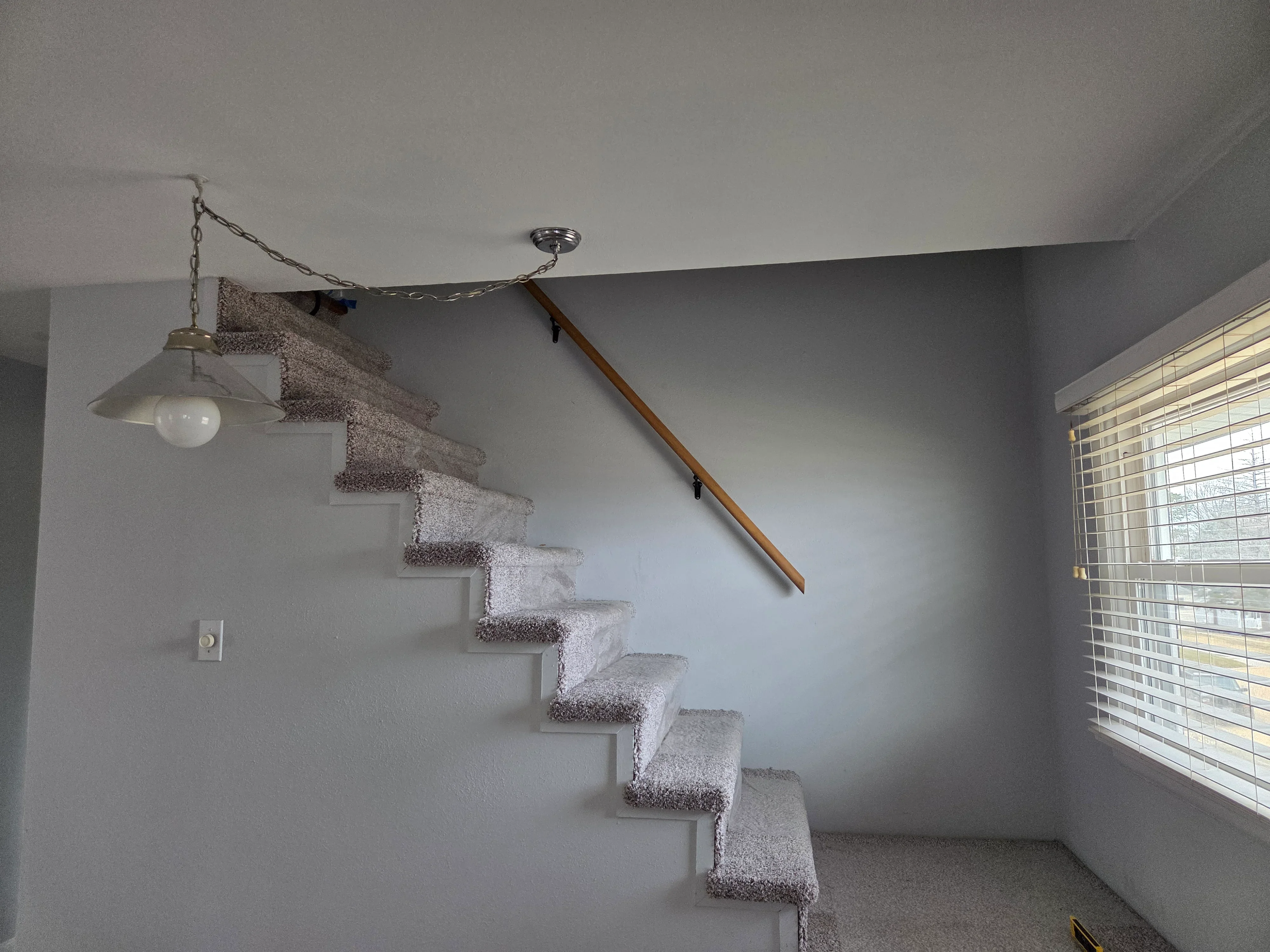 Carpeted staircase with wooden handrail, metal brackets, and pendant light fixture