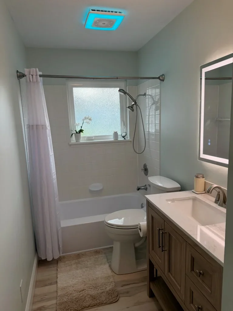 Renovated bathroom with tile shower, dual sink vanity, LED mirror, and blue ceiling exhaust fan