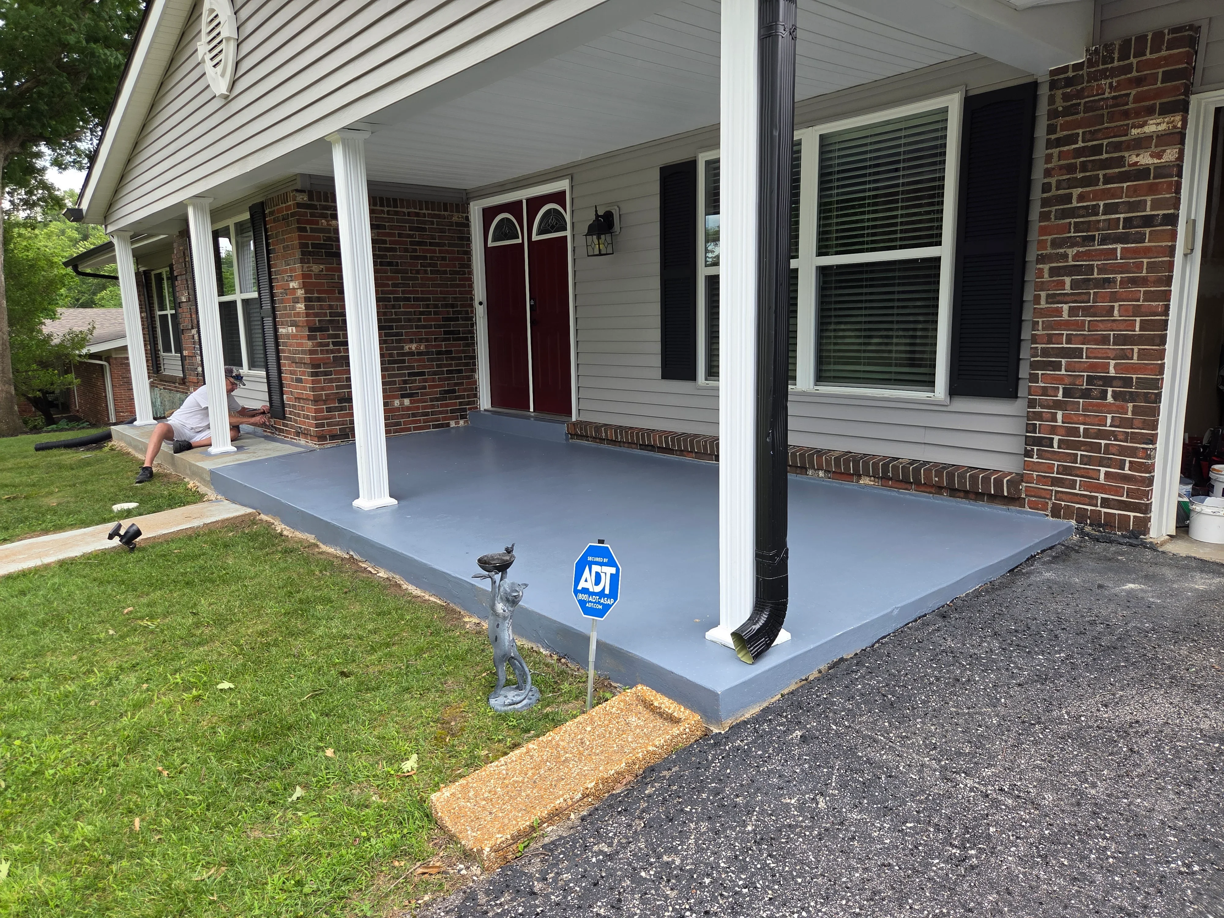 Gray concrete porch with white support columns, brick exterior, and new drainage system installation