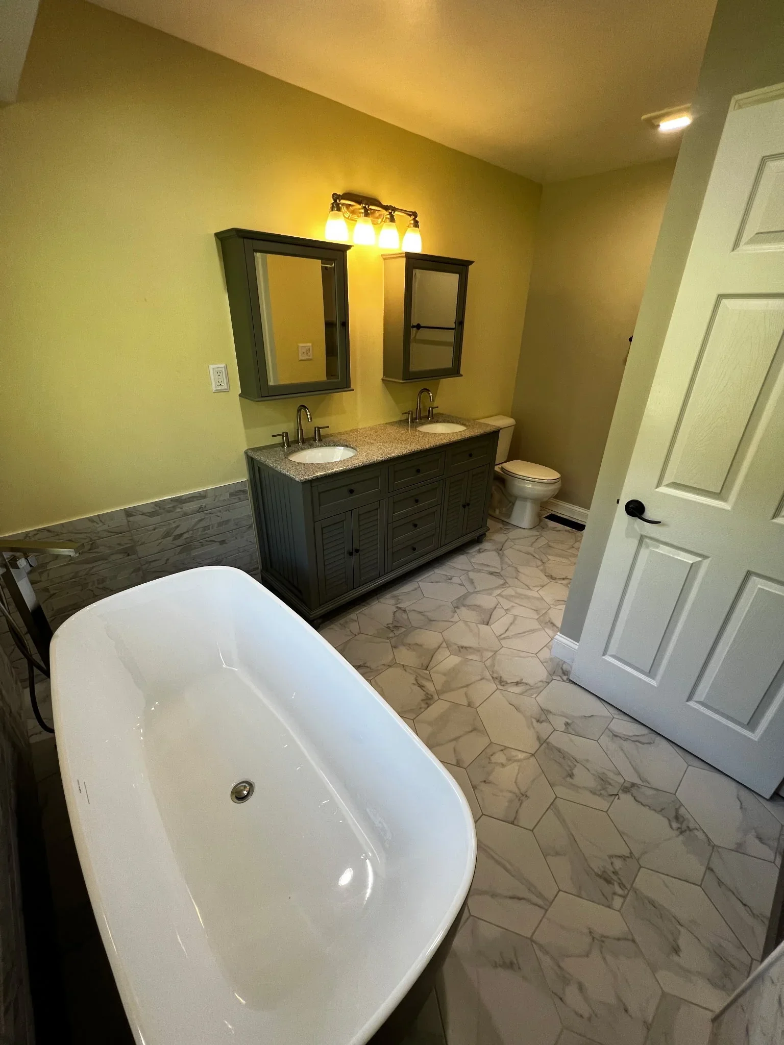 Renovated bathroom with freestanding tub, dual vanity, granite counters, and hexagonal tile flooring