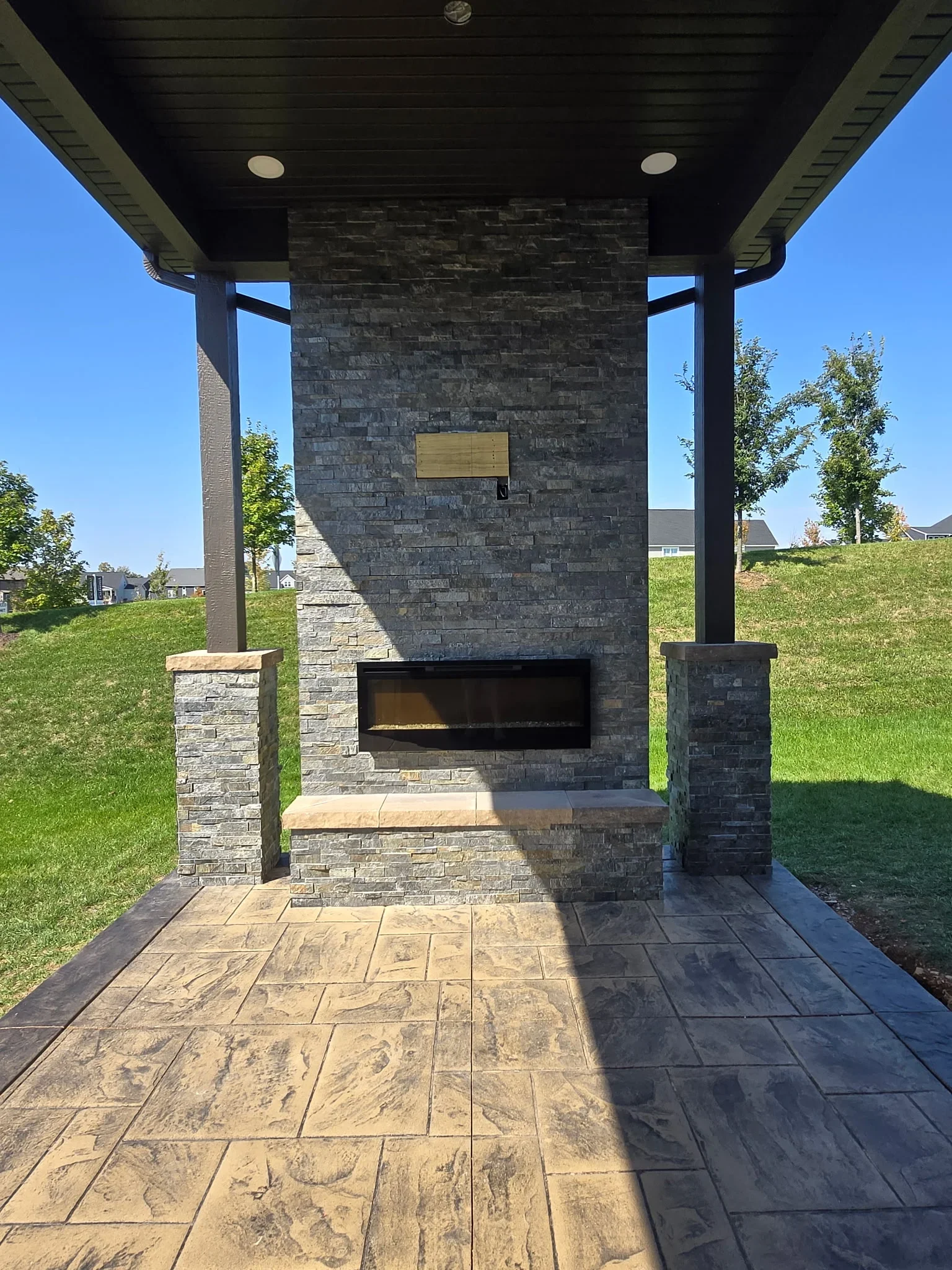 Stacked stone fireplace with linear insert, stone seating, covered patio with steel beams and stamped concrete