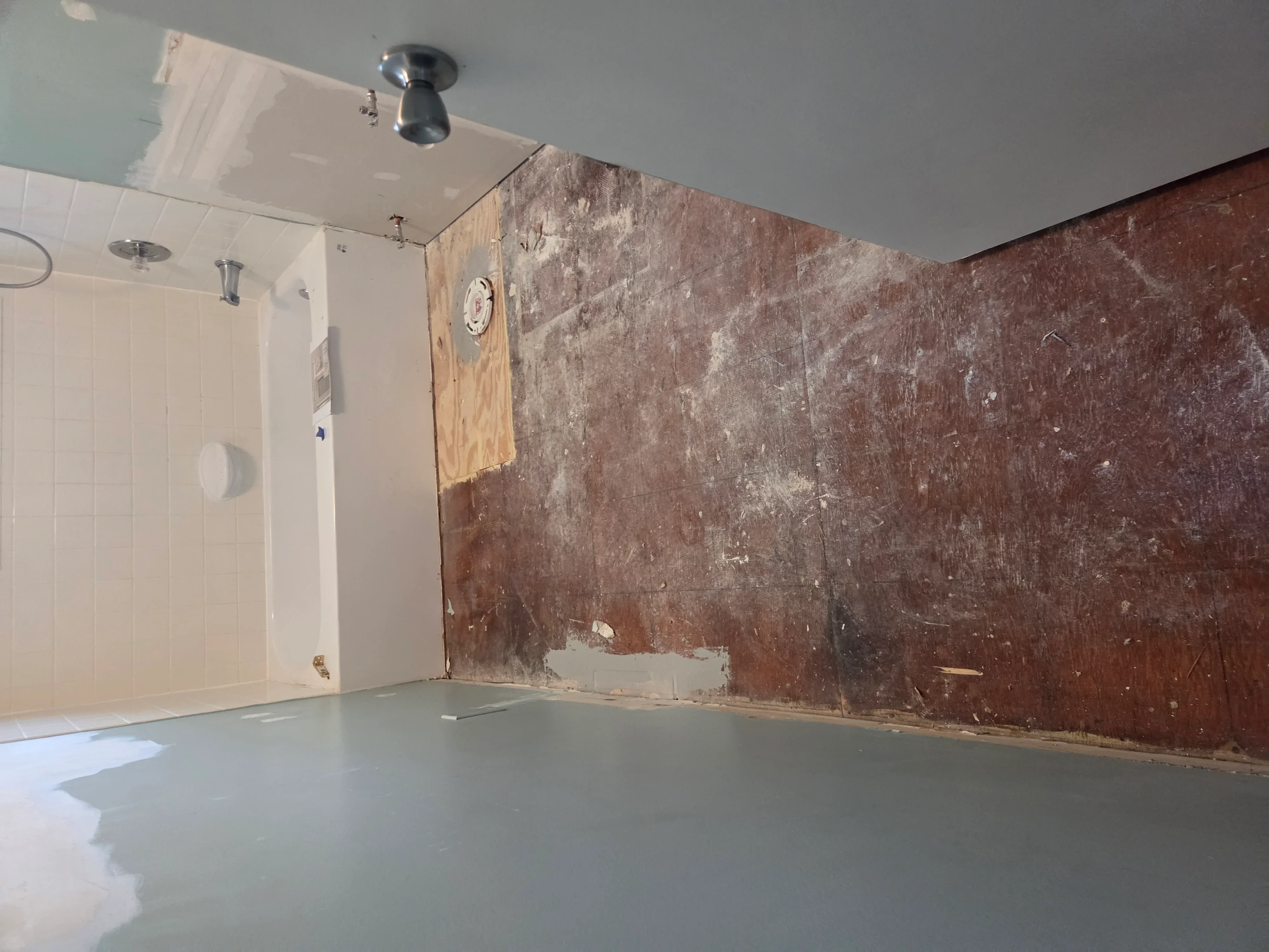 Bathroom under renovation with new drywall, ceramic tile shower surround, and painted ceiling