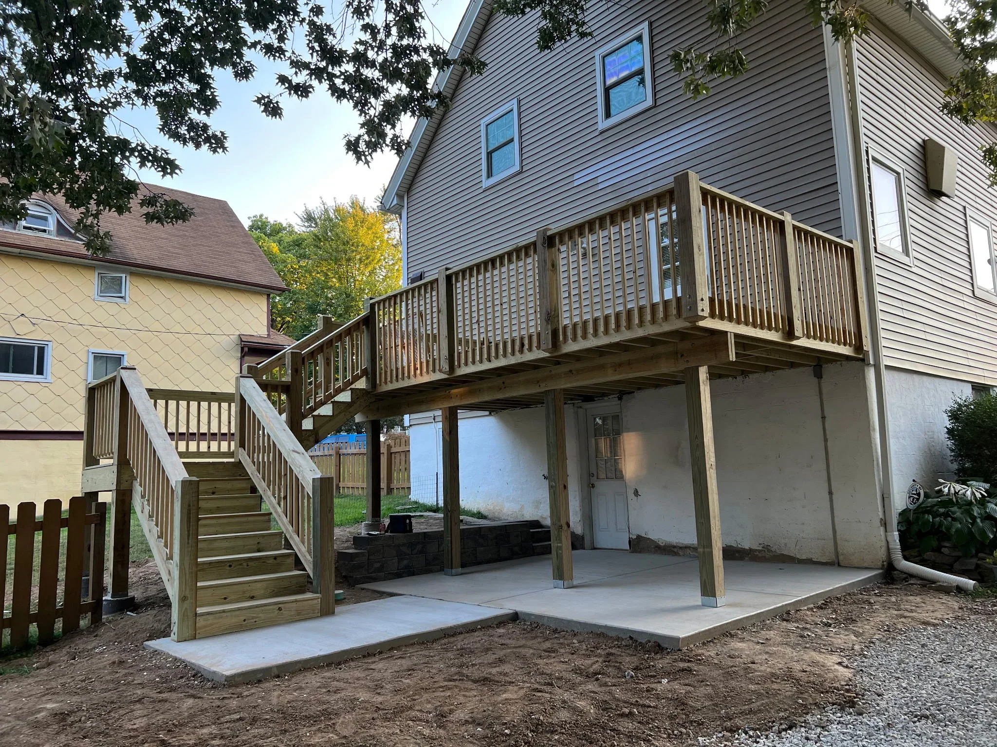 Two-story wood deck with stairs and railings above concrete patio with overhead structure