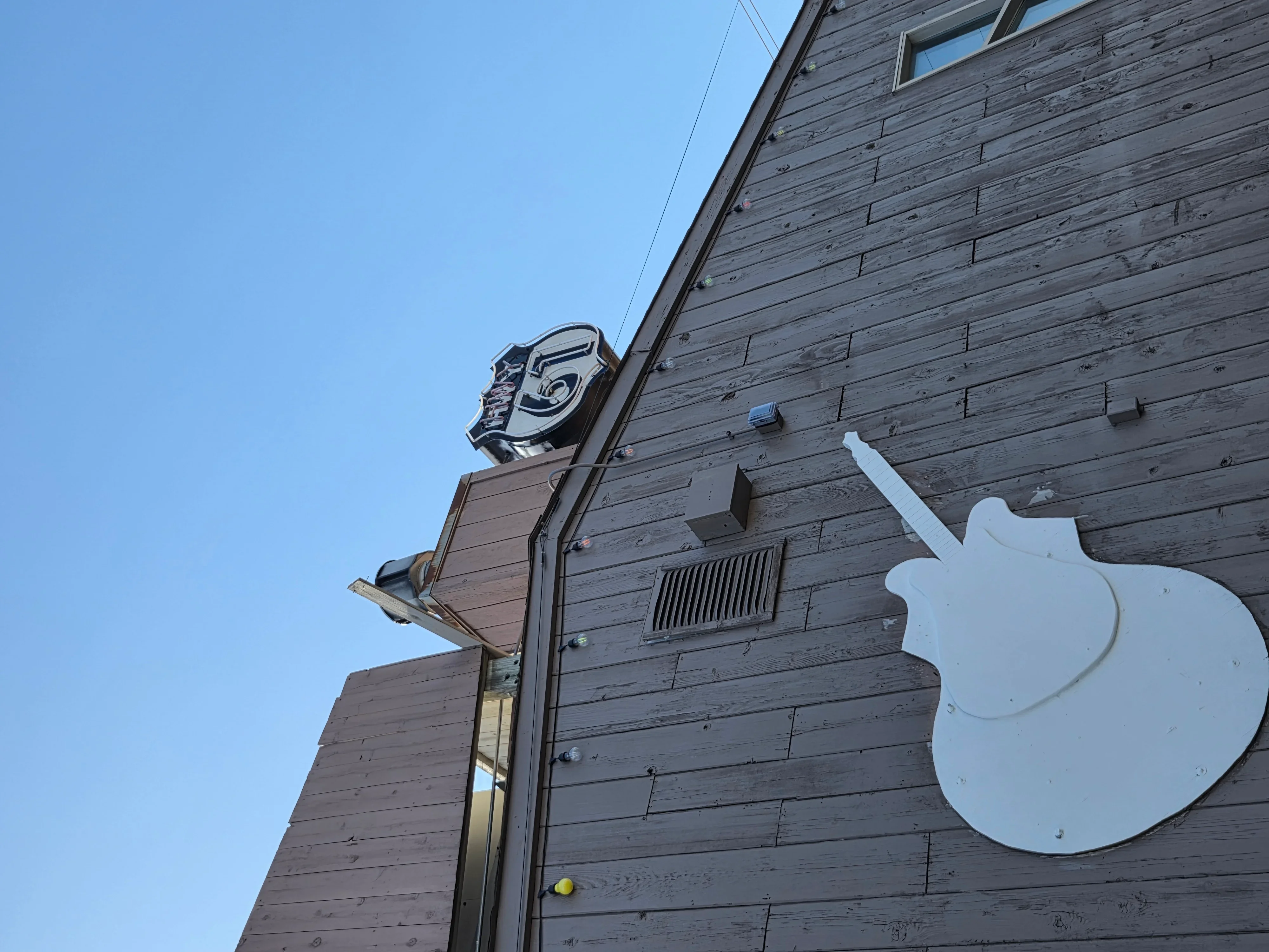 White dimensional sign and metal rooftop sign mounted on horizontal wood siding building facade